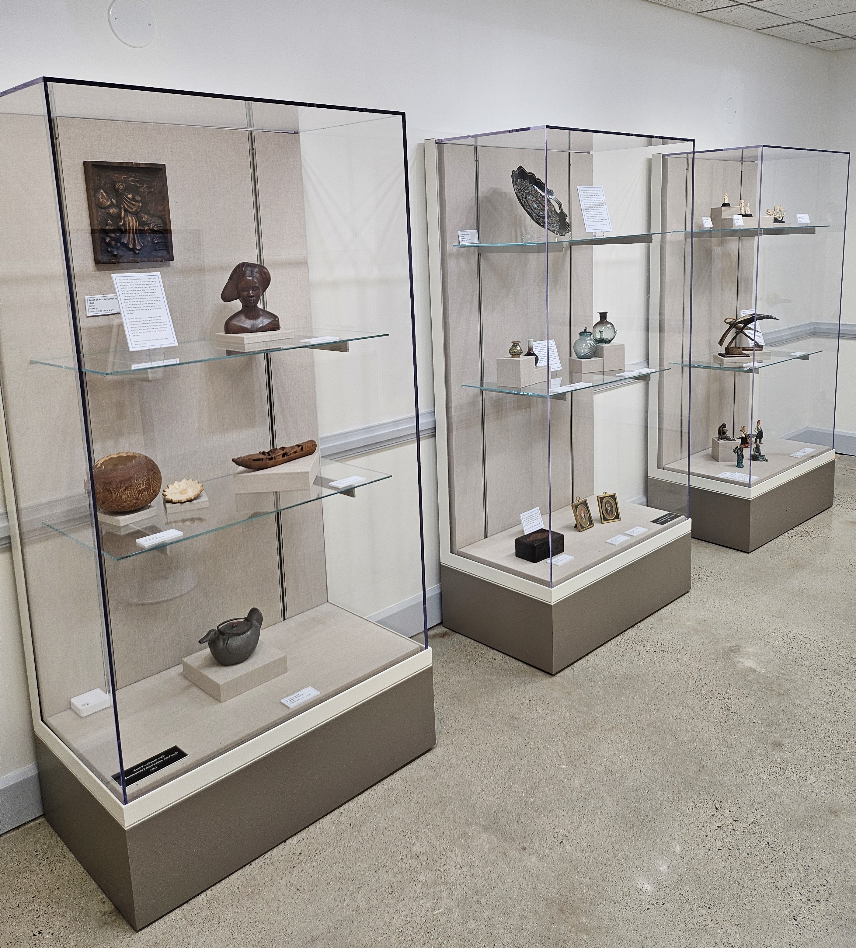 Three museum cases displaying glassware, ivory sculptures, woodcuts, and other travel mementos.